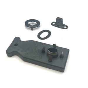 May include: A black plastic tool for installing snap fasteners. The tool has a handle and a set of dies for different sizes of snaps. There are also four separate snap fasteners, including a black metal snap, a black metal washer, and a black metal base.