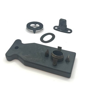 May include: A black plastic tool for installing snap fasteners. The tool has a handle and a set of dies for different sizes of snaps. There are also three separate pieces: a black metal snap, a black metal washer, and a black metal base.