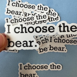 Peut inclure: Un tas d'autocollants blancs avec du texte noir qui dit "I choose the bear". Les autocollants sont sur un fond bleu clair.