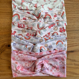 May include: Set of five pink and white patterned headbands. The headbands feature different designs, including rainbows, smiley faces, and flowers.