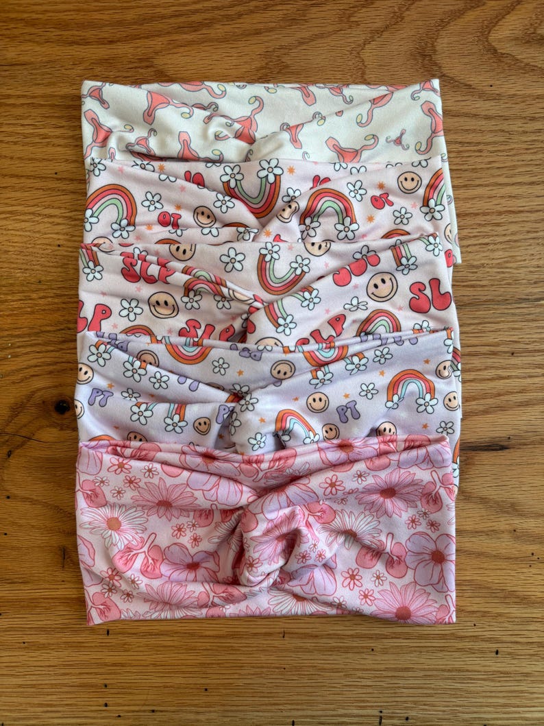 May include: Set of five pink and white patterned headbands. The headbands feature different designs, including rainbows, smiley faces, and flowers.