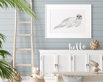May include: A framed watercolor print of a seal in a white frame hangs on a light blue wall. A white cabinet with shuttered doors and a wooden ladder are in the foreground. A woven basket with a teddy bear and the word "hello" are also visible.
