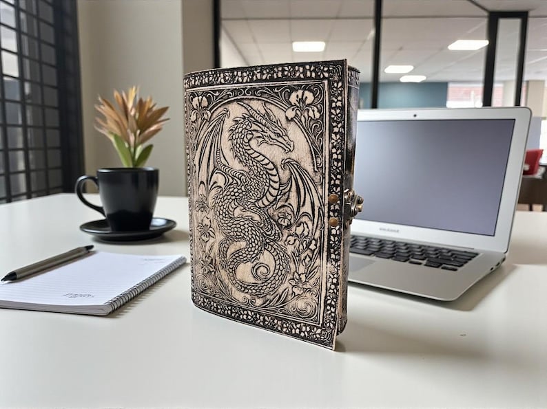 May include: A leather-bound journal with a detailed dragon design. The cover features an embossed dragon with intricate wing and scale details, surrounded by floral patterns. The journal is closed with a metal clasp.