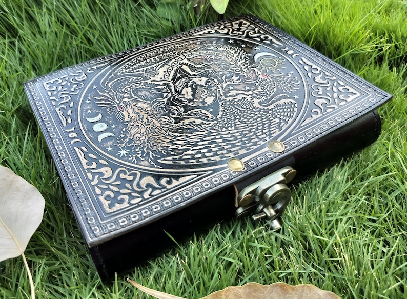 May include: Black leather journal with a silver embossed design of a tree, a bird, and a moon. The journal has a metal clasp.