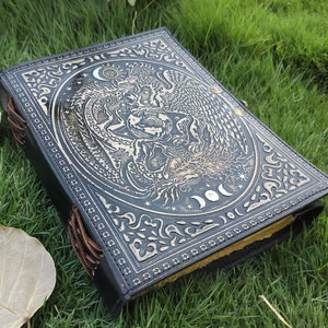 May include: Black leather journal with an embossed design of a phoenix and a dragon with moons and stars. The journal has brown leather ties.