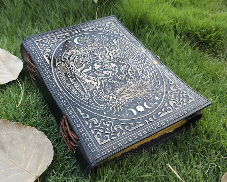 May include: Black leather journal with an embossed design of a phoenix and a dragon with moons and stars. The journal has brown leather ties.