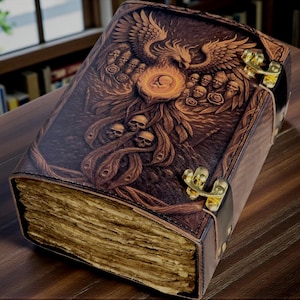 Peut inclure: Un grand livre en cuir marron avec des gravures complexes. La couverture présente un phénix, des crânes et d'autres motifs détaillés. Le livre a des fermoirs dorés et des pages jaunies, suggérant un thème vintage ou fantastique.