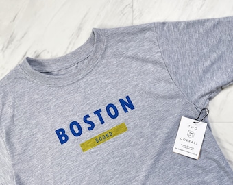 May include: Gray t-shirt with the text "BOSTON BOUND" in blue and yellow lettering.