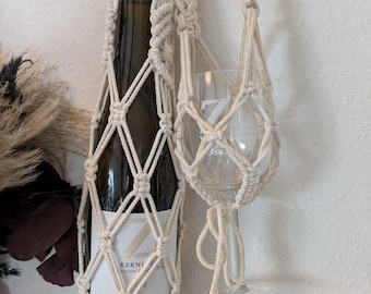 Puede incluir: Un porta botellas y vasos de macramé blanco con una botella de vino blanco dentro. La etiqueta de la botella dice "Zahn Kernwein" y "Zahn".