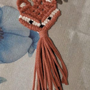 May include: A handmade fox keychain in shades of coral, white, and black. The fox head is crocheted with a detailed design, featuring a tassel tail. The keychain is attached to a gold-colored clasp with keys.