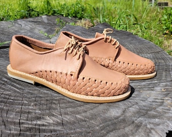 Könnte beinhalten: Ein Paar hellbraune Lederschuhe mit einem geflochtenen Lederdesign an Zehen und Seiten. Die Schuhe haben einen Schnürverschluss und eine hellbraune Ledersohle.
