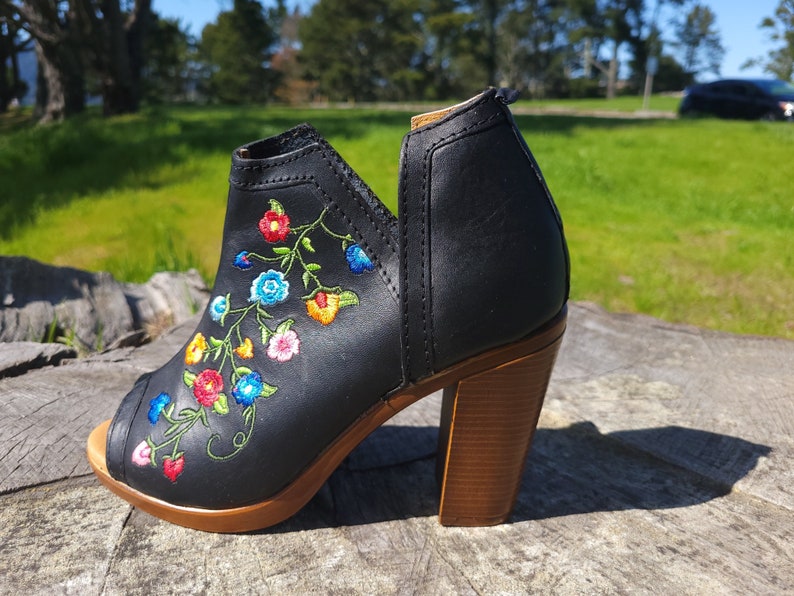 May include: Black leather peep-toe heeled bootie with colourful floral embroidery. The bootie has a wooden heel and a peep-toe design.