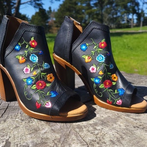 May include: A pair of black leather heeled sandals with a peep toe and floral embroidery in shades of red, blue, yellow, and pink.