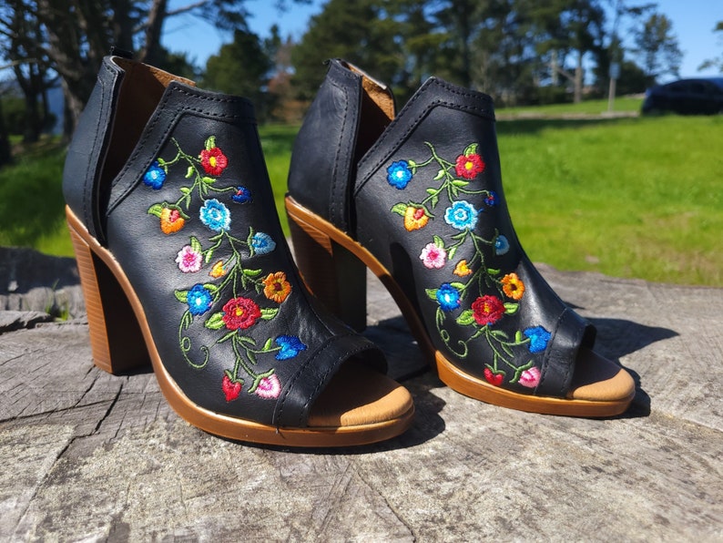 May include: A pair of black leather heeled sandals with a peep toe and floral embroidery in shades of red, blue, yellow, and pink.