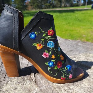 May include: Black peep-toe heeled ankle boot with a floral embroidery design. The embroidery features colourful flowers in shades of blue, red, yellow, and green.