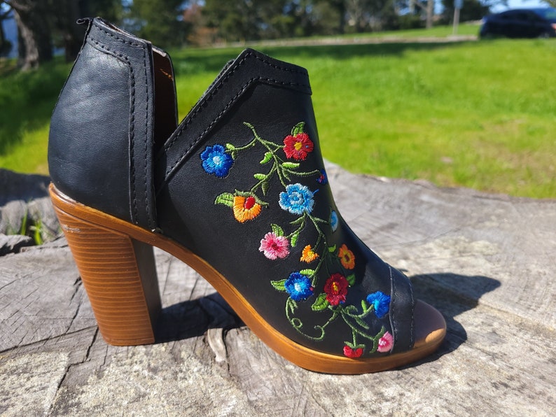May include: Black peep-toe heeled ankle boot with a floral embroidery design. The embroidery features colourful flowers in shades of blue, red, yellow, and green.
