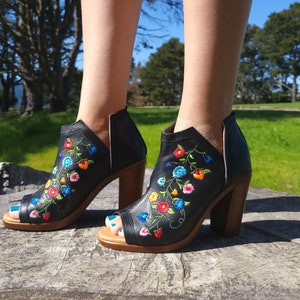 May include: Black peep-toe heeled ankle boots with colourful floral embroidery. The boots have a chunky heel and a side zipper.