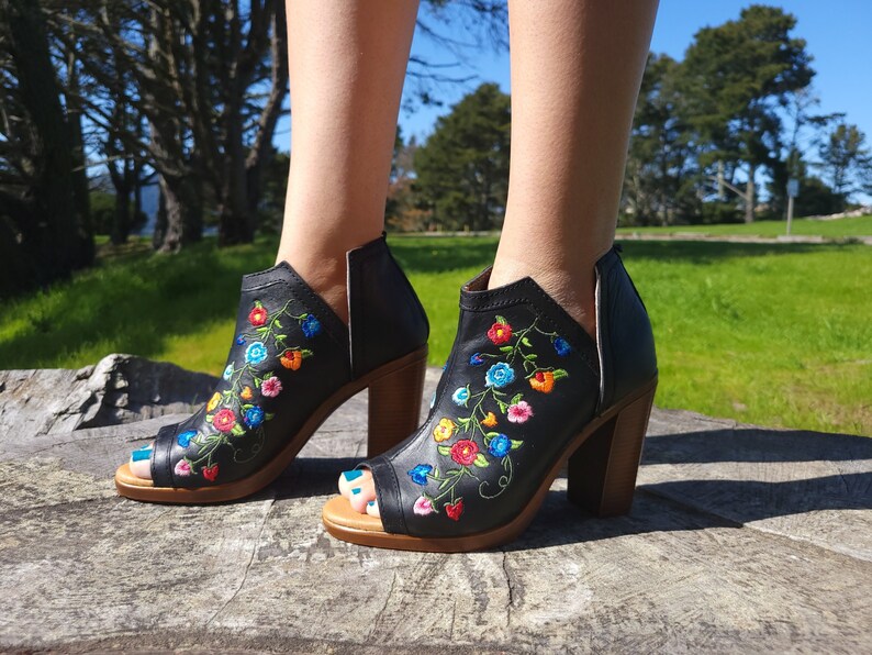 May include: Black peep-toe heeled ankle boots with colourful floral embroidery. The boots have a chunky heel and a side zipper.