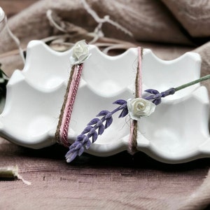 Könnte beinhalten: Ein weißer Keramik-Eierkarton mit einem Lavendelzweig und weißen Papierblumen, die mit Schnur und rosa Band gebunden sind.