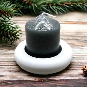 May include: A dark grey candle with a white ring base. The candle is sitting on a wooden surface.