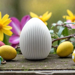 Può includere: Un uovo decorativo bianco, con scanalature verticali, è il punto focale di questa immagine. Due uova gialle macchiate e fiori colorati circondano l'uovo, posto su una superficie di legno invecchiato. Lo sfondo è sfocato, creando un'ambientazione morbida e naturale.