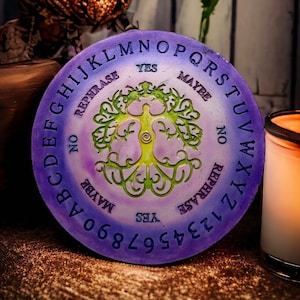 Puede incluir: Una tabla de Ouija morada y verde con un diseño de árbol de la vida. La tabla tiene letras, números y las palabras "Sí", "No", "Tal vez" y "Reformular".
