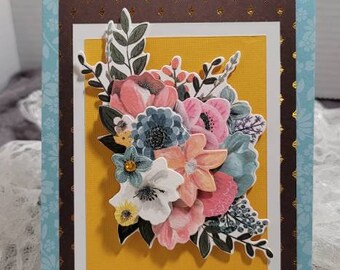 May include: A handmade card with a blue and brown border and a yellow background. The card features a bouquet of colorful flowers with a 3D effect.