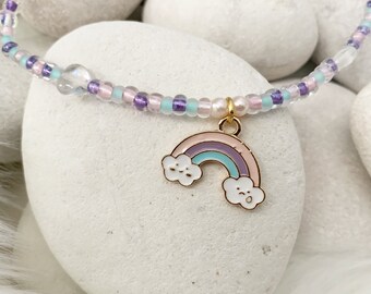 May include: A delicate beaded bracelet with a rainbow charm. The rainbow is pink, purple, blue, and green with white clouds. The beads are white, pink, purple, and light blue.