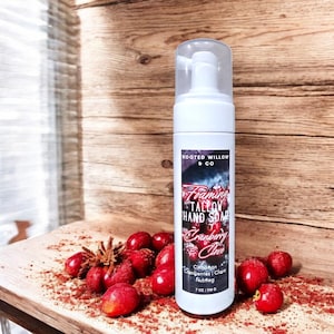 Könnte beinhalten: Weiße, schäumende Handseifenflasche mit transparentem Pumpkopf, beschriftet mit "Foaming Tallow Hand Soap Cranberry Clove". Die Flasche ist von frischen Cranberries und Gewürzen umgeben. Die Seife ist 198 g.