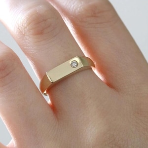 May include: A gold band ring with a single small diamond set in the center of the band.