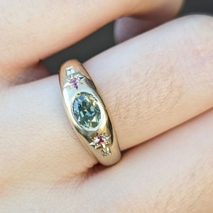 Op de afbeelding: Een gouden ring met een groene ovale edelsteen omringd door kleine roze en witte edelstenen.