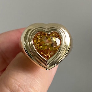May include: A gold heart-shaped ring with a large, faceted, yellow gemstone in the centre.