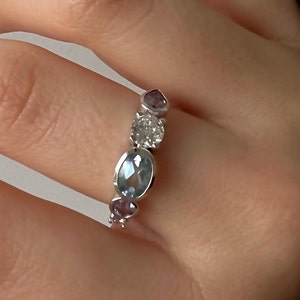 Op de afbeelding: Een zilveren ring met een cluster van ovale en ronde edelstenen. De ring bevat een grote ovale aquamarijn, een ronde diamant en twee kleinere ovale amethiststenen.