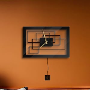 May include: A black modern wall clock with gold hands and a geometric design. The clock is hanging on an orange wall above a brown leather sofa with orange cushions.
