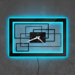 以下が含まれることがあります： ローマ数字と銀色の針を持つ黒い時計は、一連の黒い正方形で囲まれています。時計は青いネオンライトで照らされています。