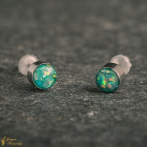May include: Two silver stud earrings with green opal-like stones. The stones have a shimmery, iridescent finish.