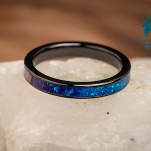 May include: A black ceramic ring with a thin band of blue and pink opal inlay.