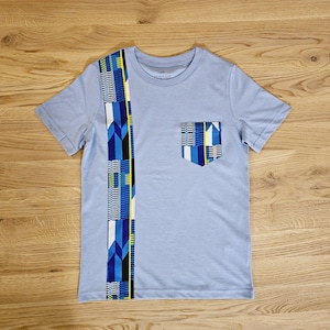 Puede incluir: Una camiseta azul claro con un bolsillo estampado y una franja vertical estampada en el lado izquierdo. El patrón es en tonos de azul, amarillo y negro.
