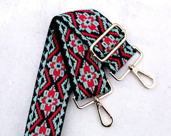 May include: A black, red, and blue patterned fabric strap with gold metal clasps. The strap is designed for a bag or purse.