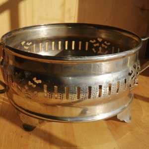 Puede incluir: Tazón de metal plateado con un diseño decorativo de corte y dos asas. El tazón se asienta sobre tres pequeños pies.