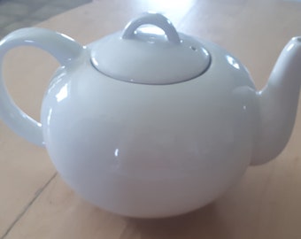 May include: A white ceramic teapot with a round body and a lid. The teapot has a handle and a spout.