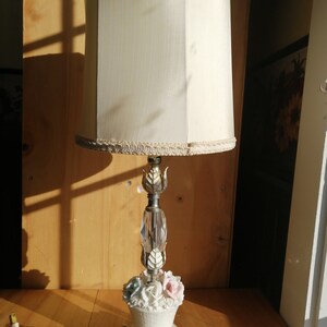Peut inclure: Une lampe de table vintage avec un abat-jour en tissu blanc et une base florale. La base présente une tige en cristal et un arrangement de fleurs en porcelaine avec des fleurs roses, bleues et blanches.