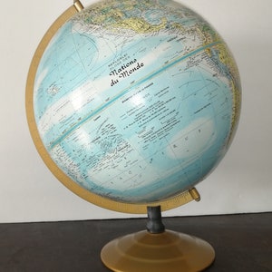 Może przedstawiać: Antyczny niebieski globus z pozłacaną podstawą i mosiężnym południkiem. Globus jest oznaczony jako "Nations du Monde" i ma średnicę 30,5 cm.