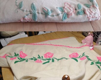 May include: Two white crocheted blankets with pink and green embroidered roses. The blankets are folded and displayed on a wooden surface.