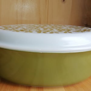 May include: A green oval casserole dish with a white lid featuring a gold floral pattern.
