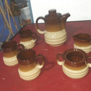 Peut inclure: Un service à thé en céramique de couleur crème et marron avec une théière, un pot à crème, un sucrier et quatre tasses.