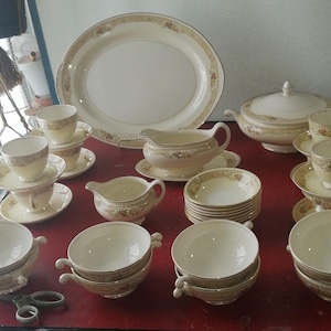 Könnte beinhalten: Ein Set vintage cremefarbenes Porzellan-Geschirr mit goldenen Verzierungen und Blumenmustern. Das Set enthält eine große Platte, eine Servierschüssel, zwei Saucieren, Teetassen, Untertassen und Schalen.