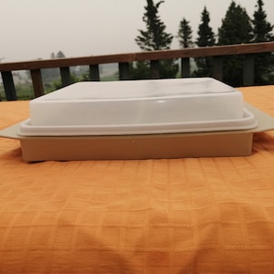 Puede incluir: Un plato para hornear rectangular de color beige con una tapa blanca. La tapa tiene un diseño de mármol.