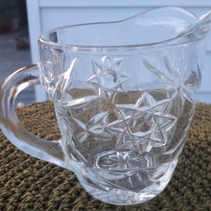 Peut inclure: Un pichet en verre transparent avec un motif en forme d'étoile. Le pichet a une poignée et un bec.