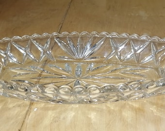 May include: A clear glass serving dish with a scalloped edge and a diamond pattern. The dish is oval shaped and has a clear, reflective surface.